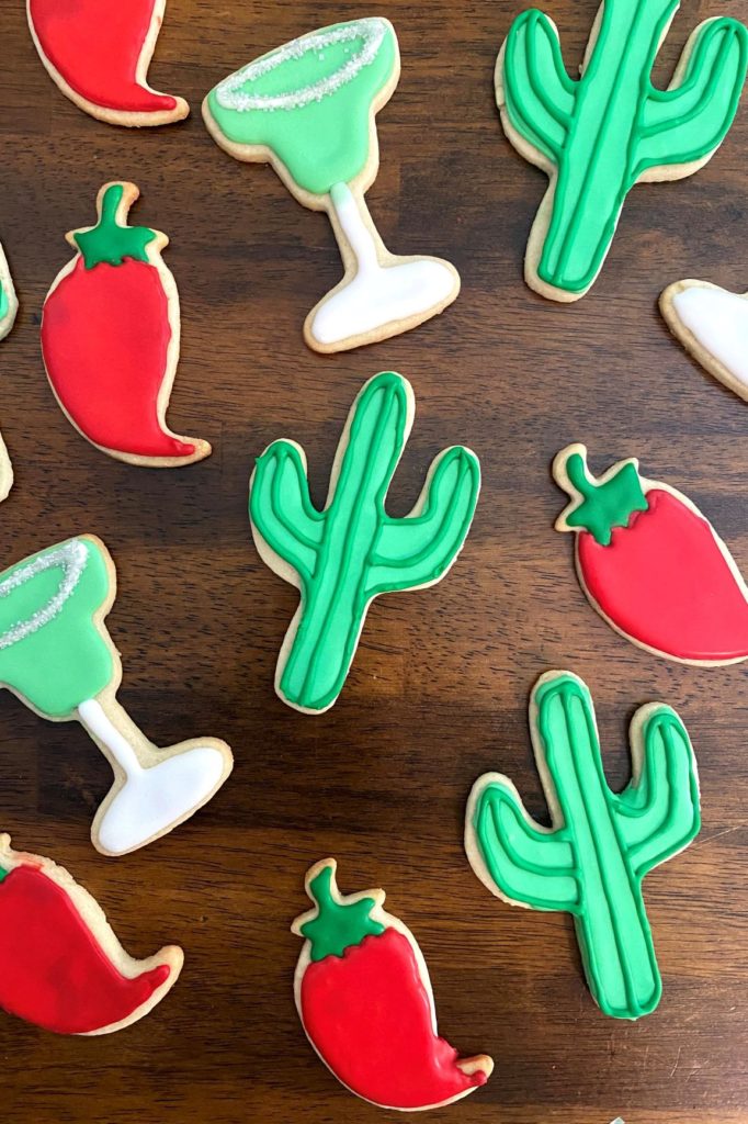 Cactus sugar cookies, margarita glass sugar cookies, and chili pepper sugar cookies displayed on a wooden table